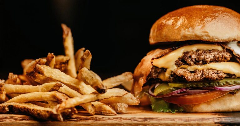 Hamburger mit Rindfleisch auf einem Holzbrett, daneben Pommes Frites.