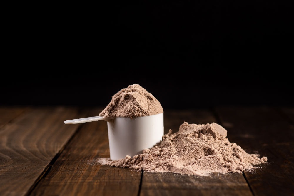 Dosierlöffel mit Whey Protein-Pulver auf einem Holztisch