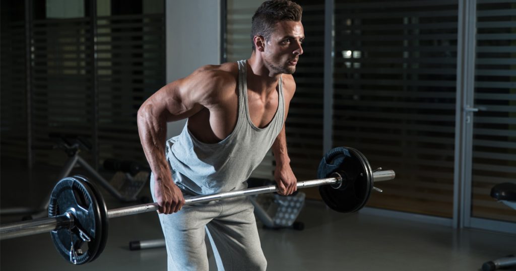 Mann im Fitness-Studio führt Langhantel-Rudern aus.