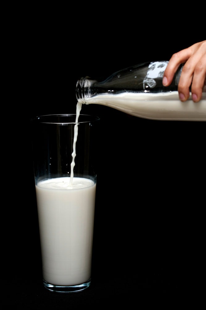 Person schenkt Milch in ein hohes Glas ein