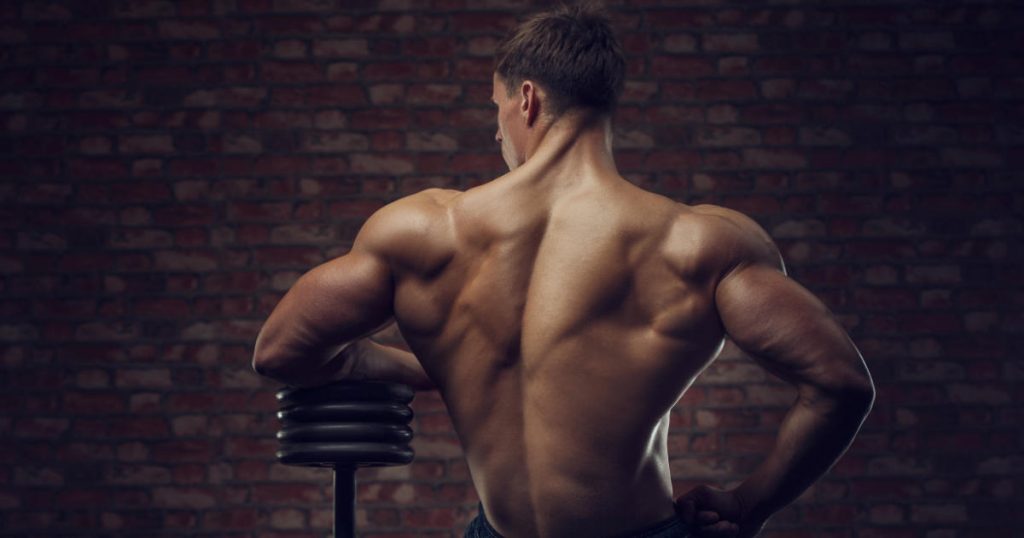 Bodybuilder mit Kurzhantel vor einer Steinwand